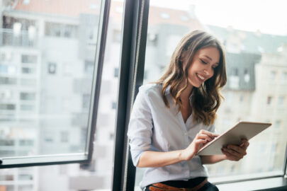 Junge Geschäftsfrau benutzt ein digitales Tablet, während sie im Büro vor Fenstern steht