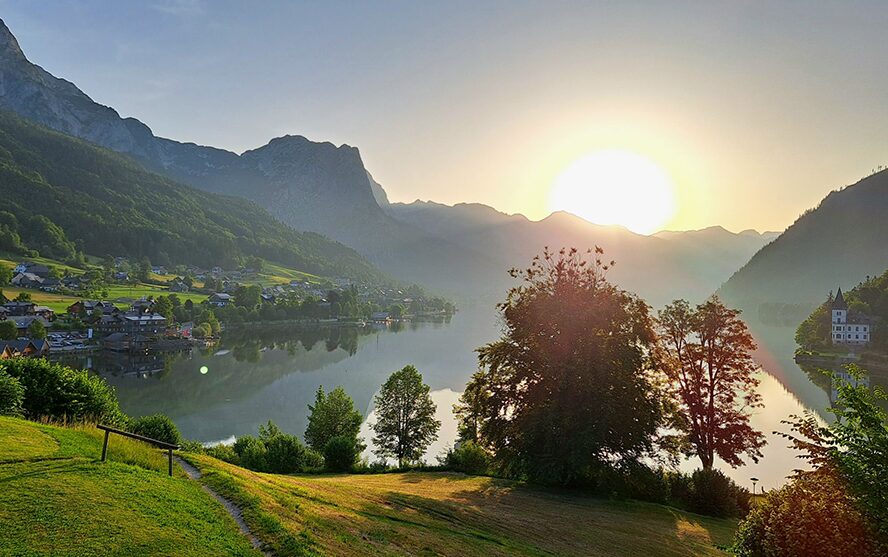 Sommerlandschaft mit Wiesen, Bäume, See und einer untergehenden Sonne