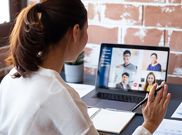 Person sitzt am Schreibtisch und nimmt an einer Videokonferenz mit fünf weiteren Teilnehmenden auf dem Laptop teil – Szene aus einem Büro- oder Homeoffice-Umfeld.