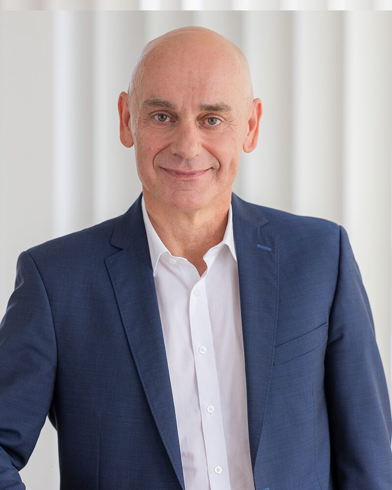 Porträt eines Mannes im blauen Sakko vor hellem Hintergrund.