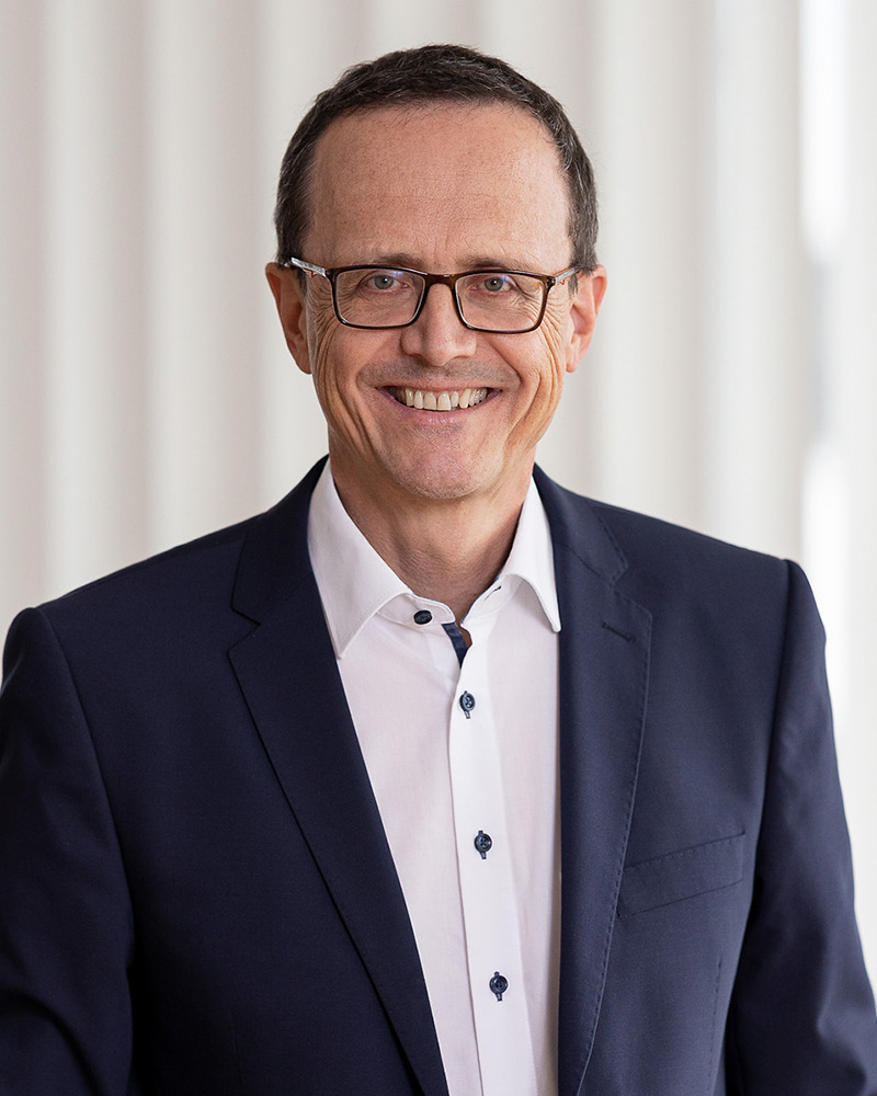 Porträt eines Mannes mit Brille im dunkelblauen Sakko, lächelnd.