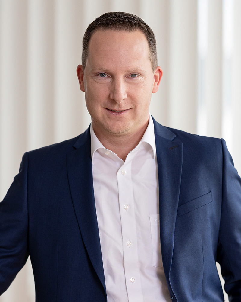 Porträt eines Mannes im blauen Sakko, heller Hintergrund, frontal.