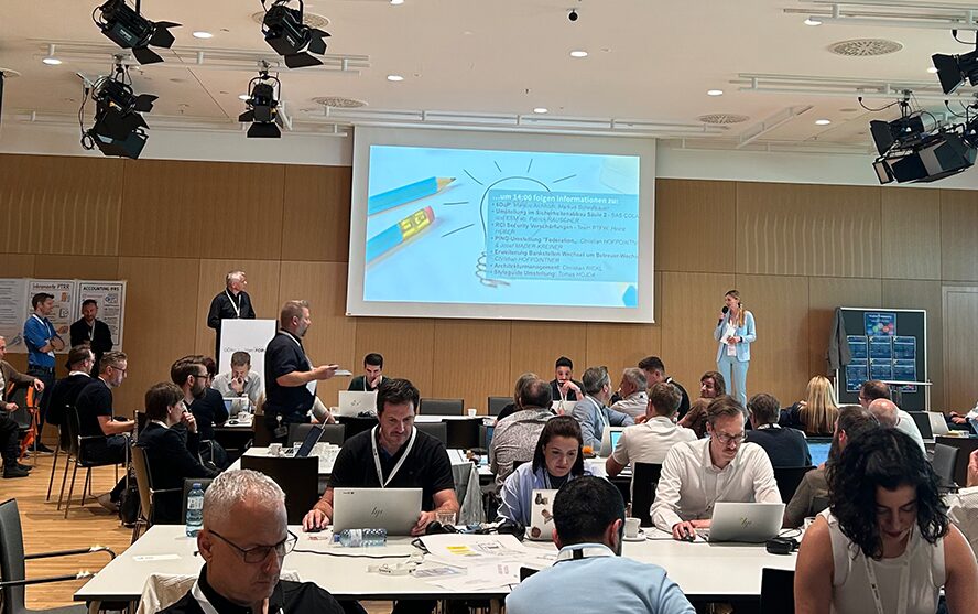 Konferenz mit Gruppenarbeit und Präsentation vor Leinwand.
